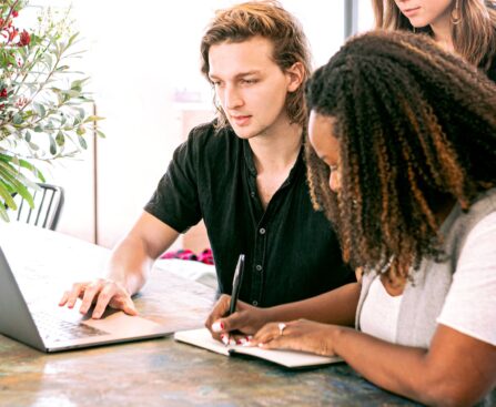 man working on laptop while woman takes notes